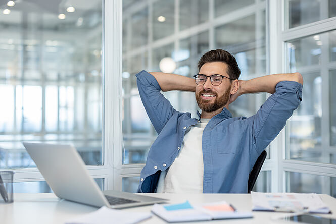Junger Mann mit Brille entspannt im modernen Büro, Pause von der Laptop-Arbeit im digitalen Arbeitsalltag